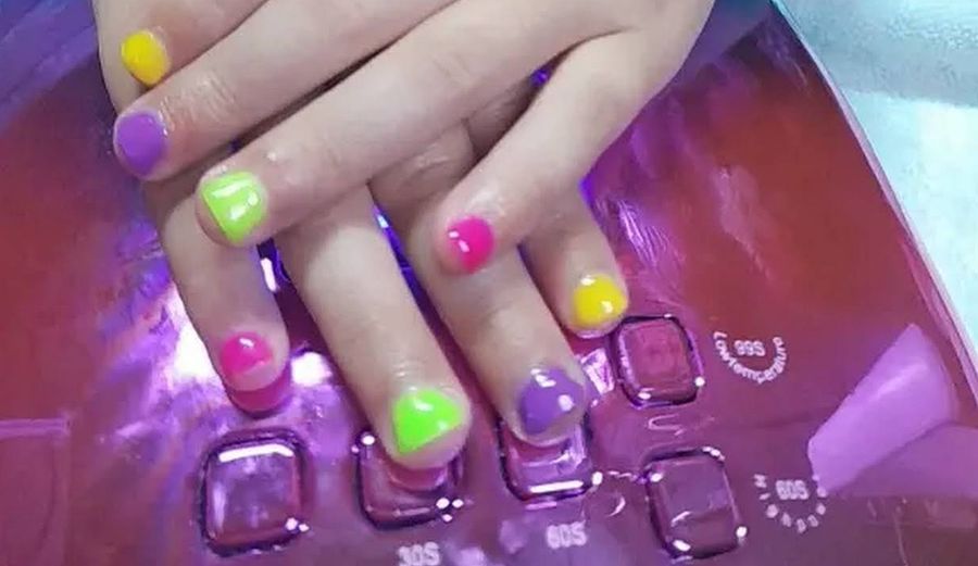 A child's hands with bright yellow, purple, green and pink gel nails