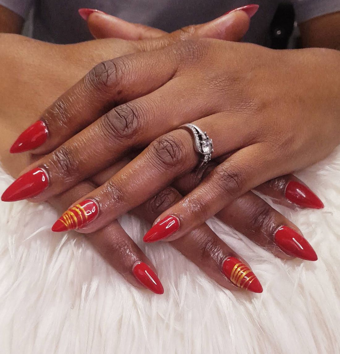 Glossy red stiletto nails with hand-painted gold stripes